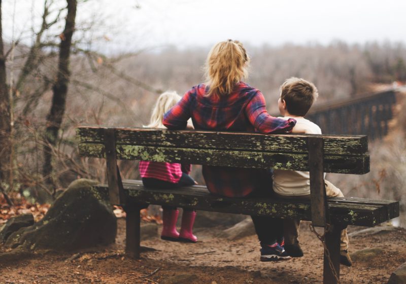 The psychological effects of being a single mother weighs on her as she sits on a bench with her kids