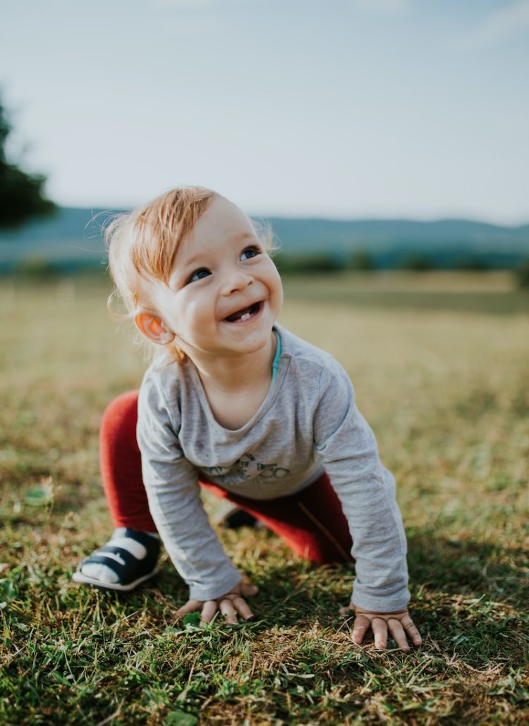 A toddler crawling on grass smiling with only two bottom teeth