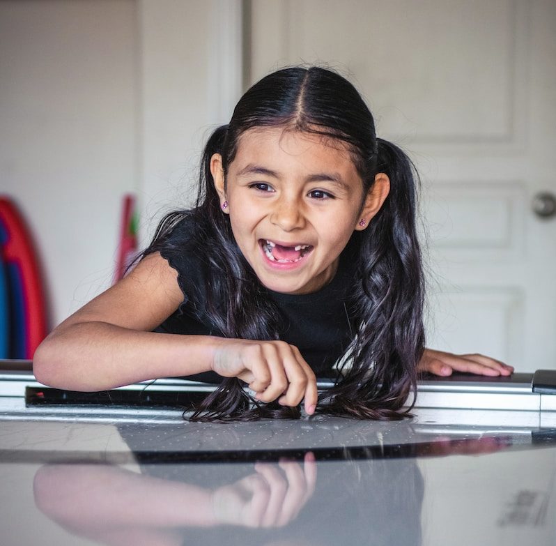 a little girl laying on top of a piano, missing many teeth and smiling wide