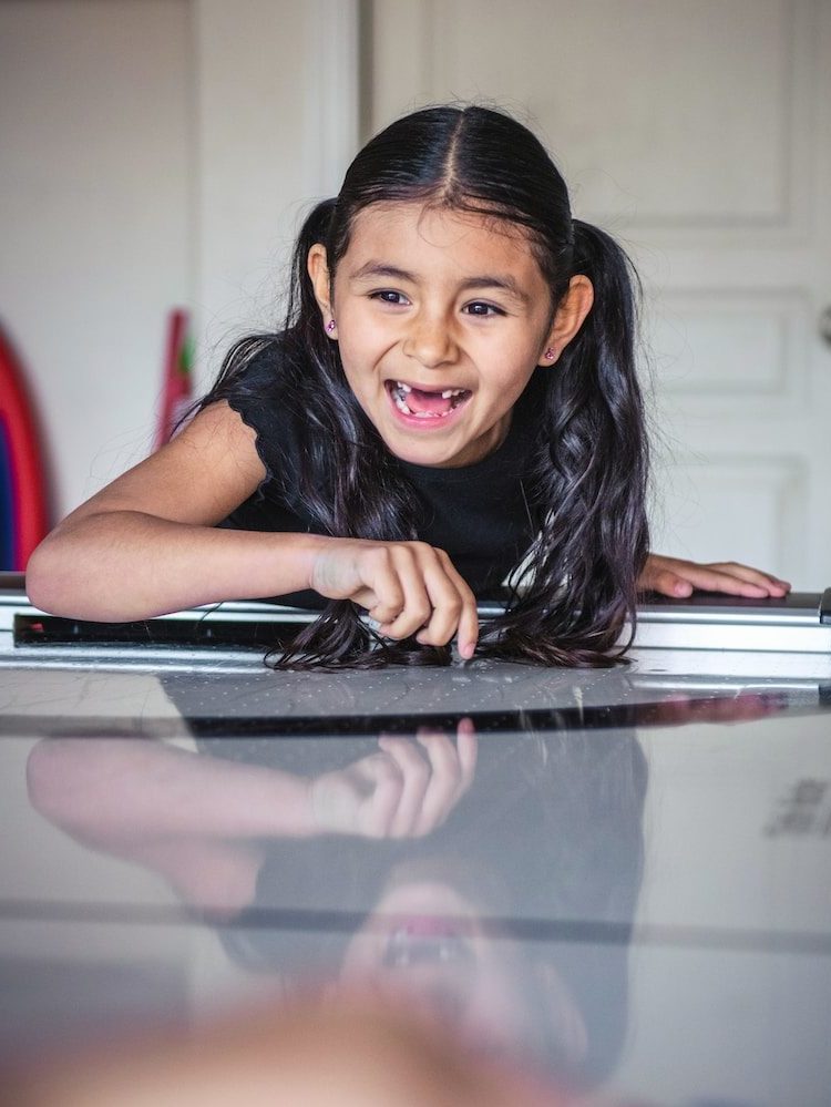 a little girl laying on top of a piano, missing many teeth and smiling wide